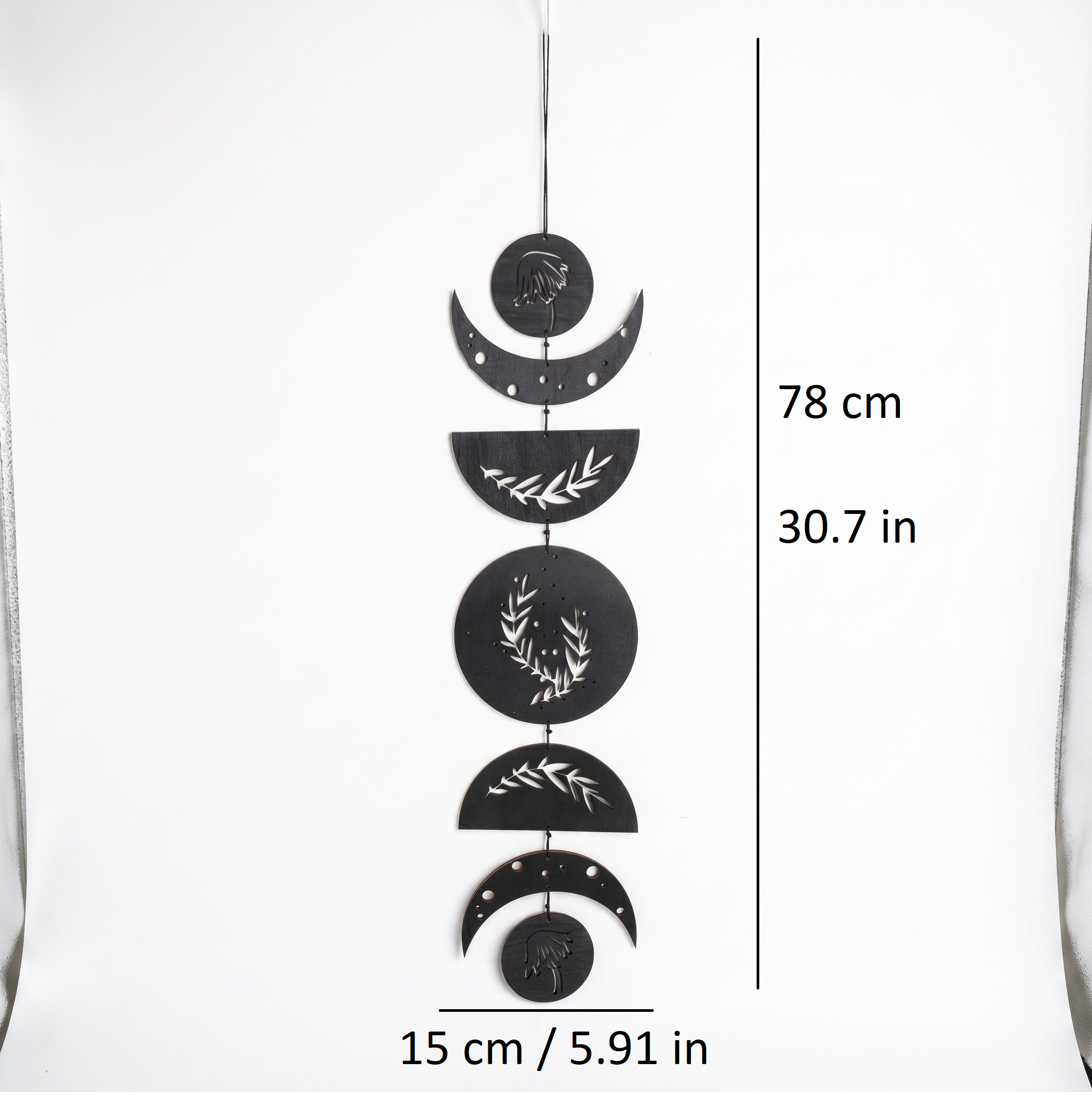 Moon phase wall hanging styled in minimalist bedroom — black boho wood art above bed