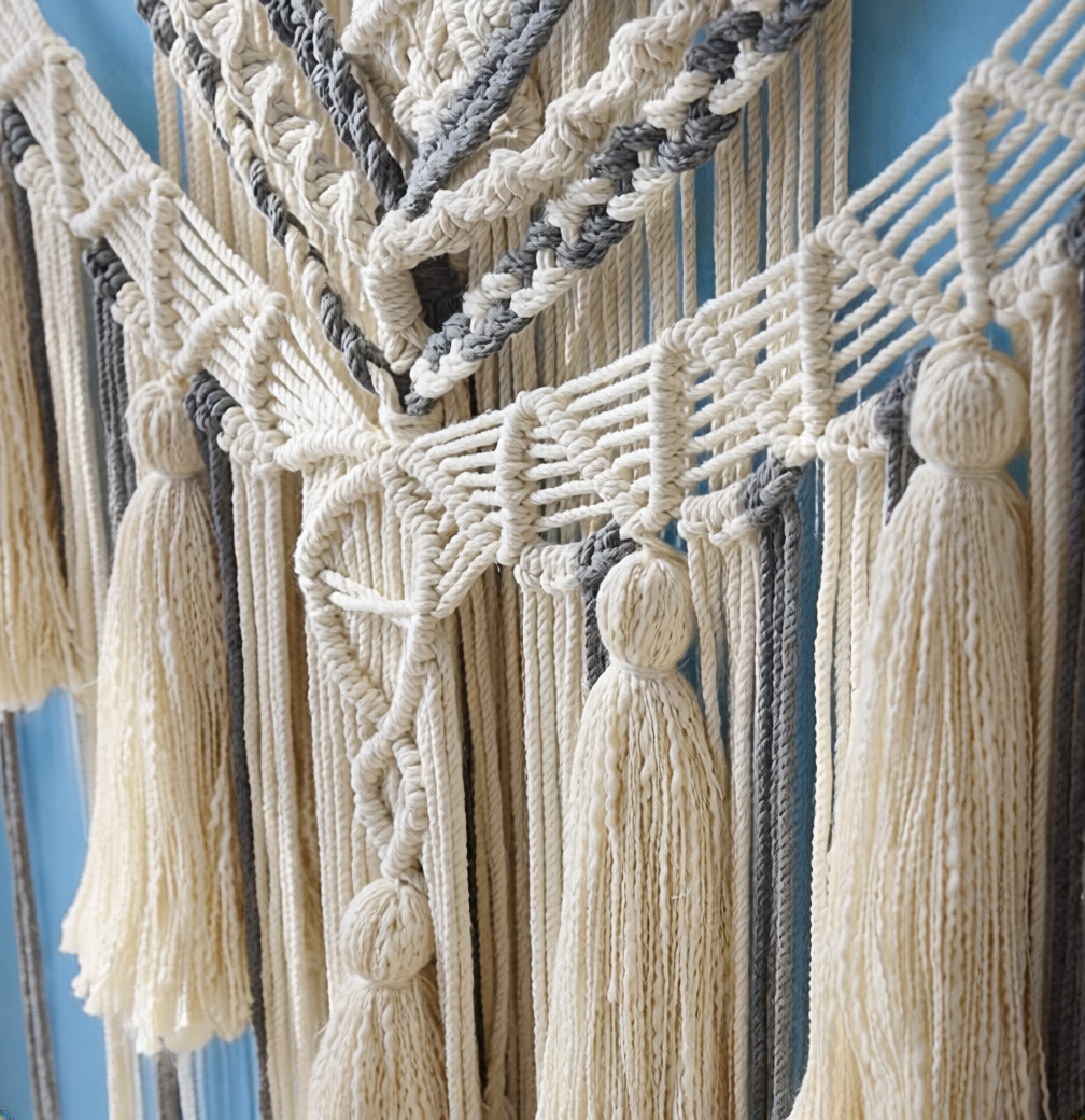 Macrame wall hanging detail — cotton cord knotwork and tassel fringe texture, cream and gray boho wall art