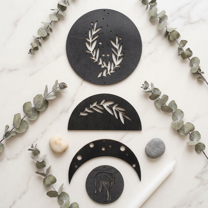 Moon phase wall art flat lay — seven matte black wooden discs on dark surface, Bohoartis