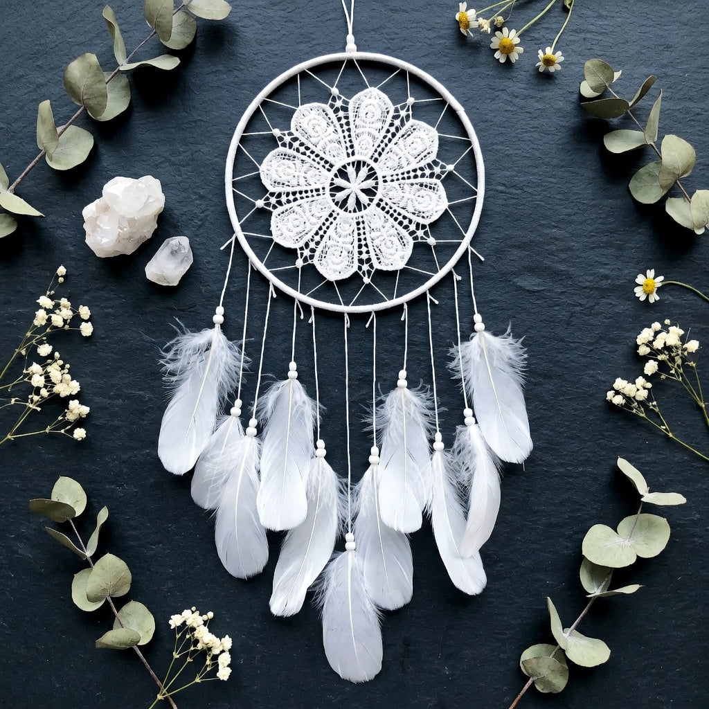 White dreamcatcher with feathers on a dark background with greenery and crystals