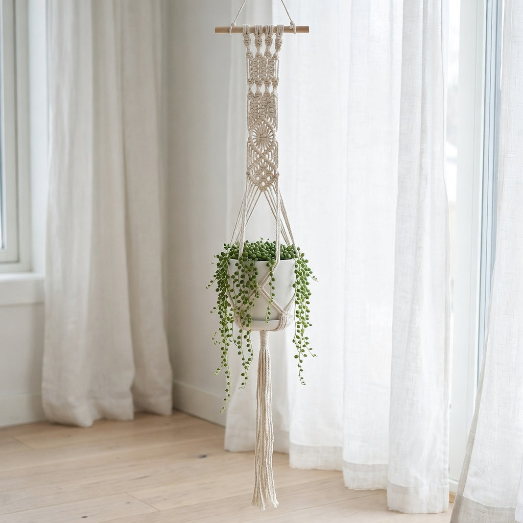 Beige cotton rope plant hanger with wooden dowel geometric weave near window in Scandinavian bedroom