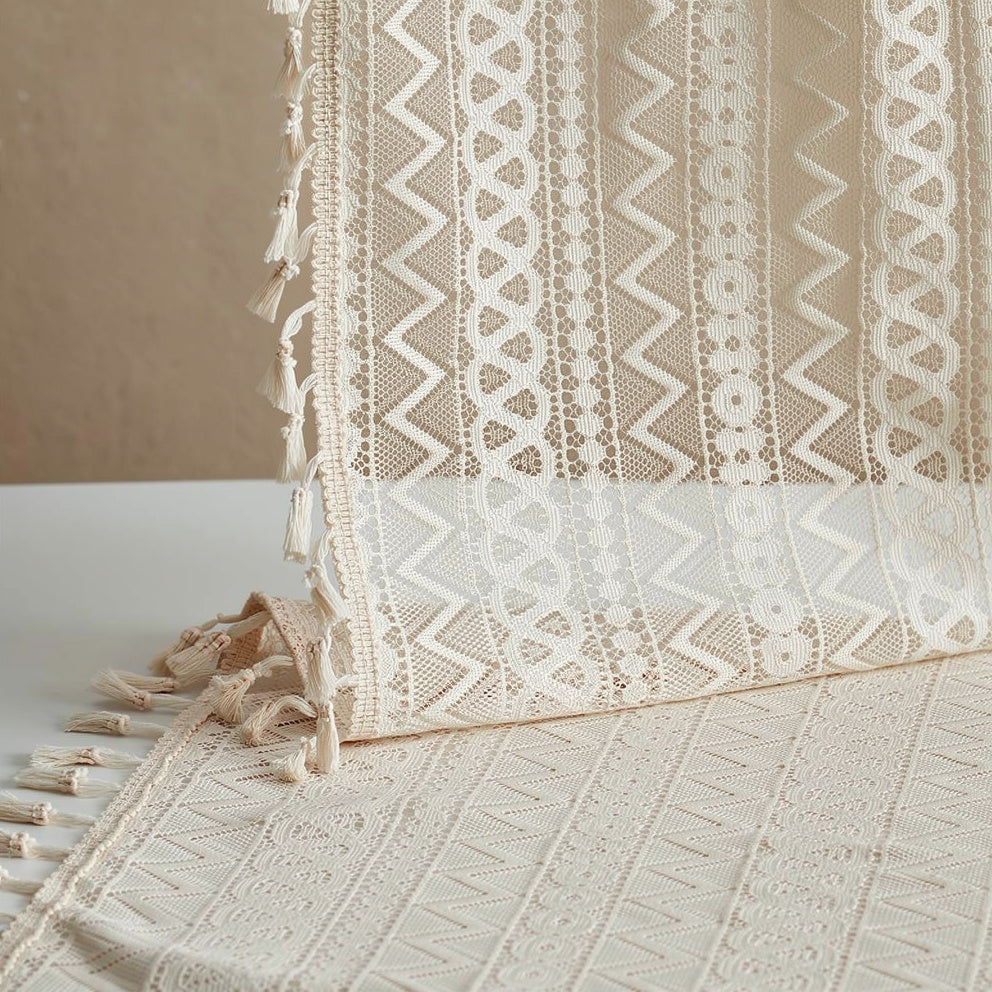Close-up of a textured beige fabric with intricate patterns and tassels on a neutral background.