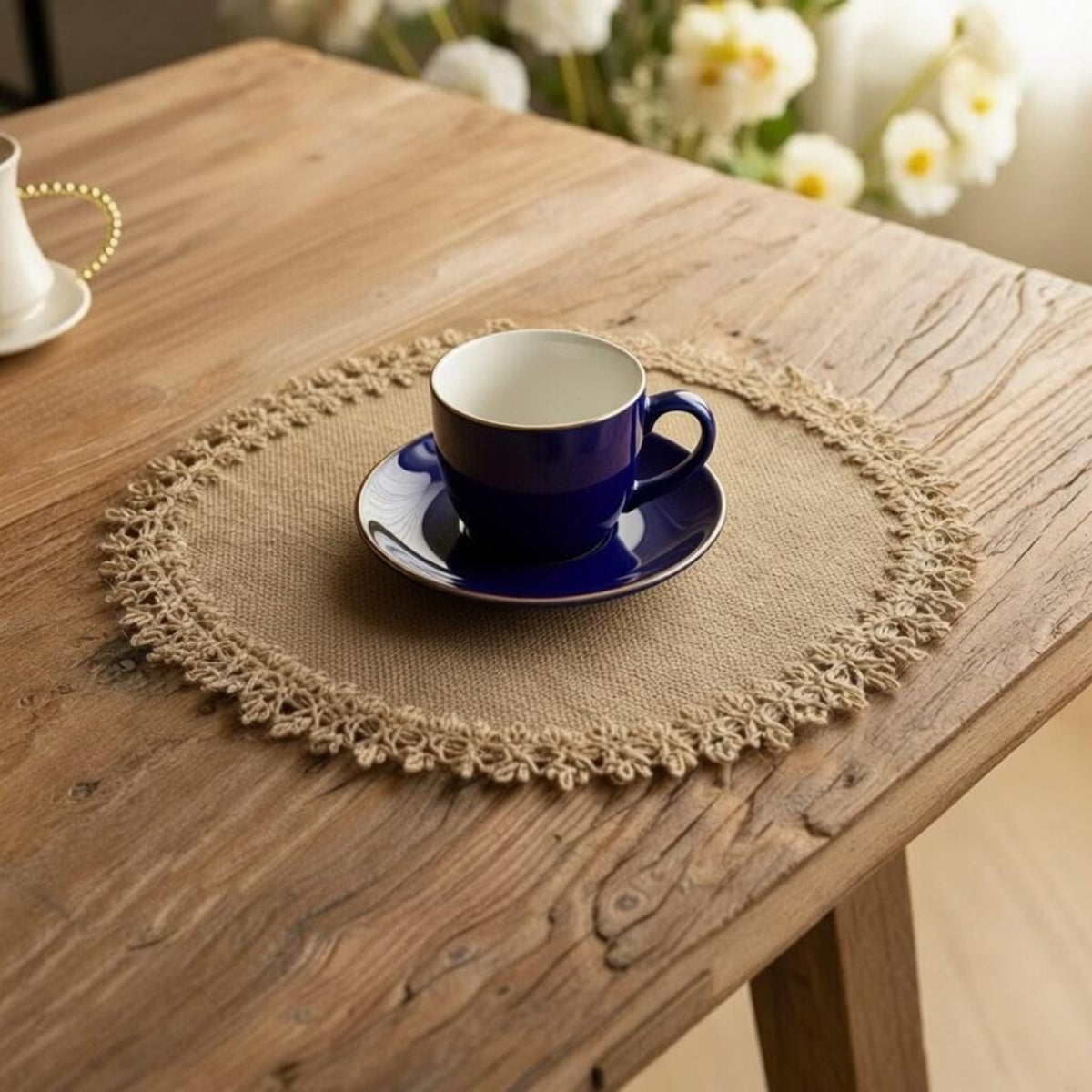 Blue ceramic cup and saucer on round burlap placemat with lace edge