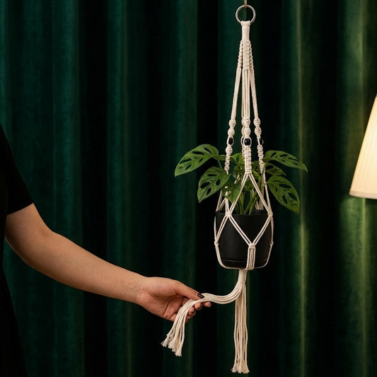 Hand holding tassel fringe of classic macrame plant hanger against dark emerald green curtain, boho decor detail