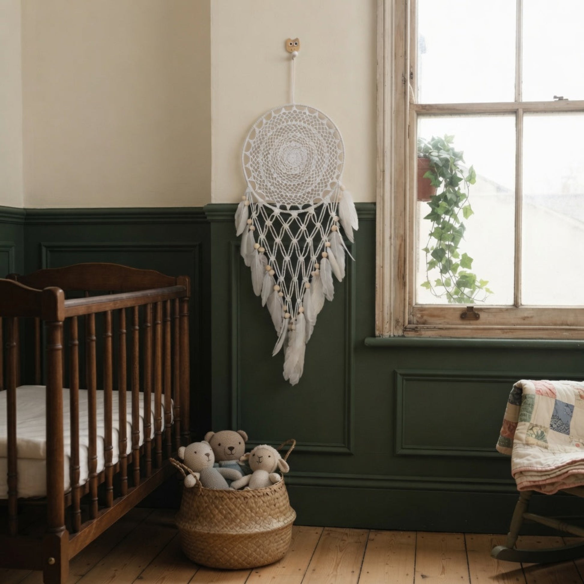 Faux feather dreamcatcher hanging in a boho nursery with green wainscoting near a wooden crib