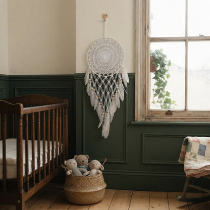 Faux feather dreamcatcher hanging in a boho nursery with green wainscoting near a wooden crib