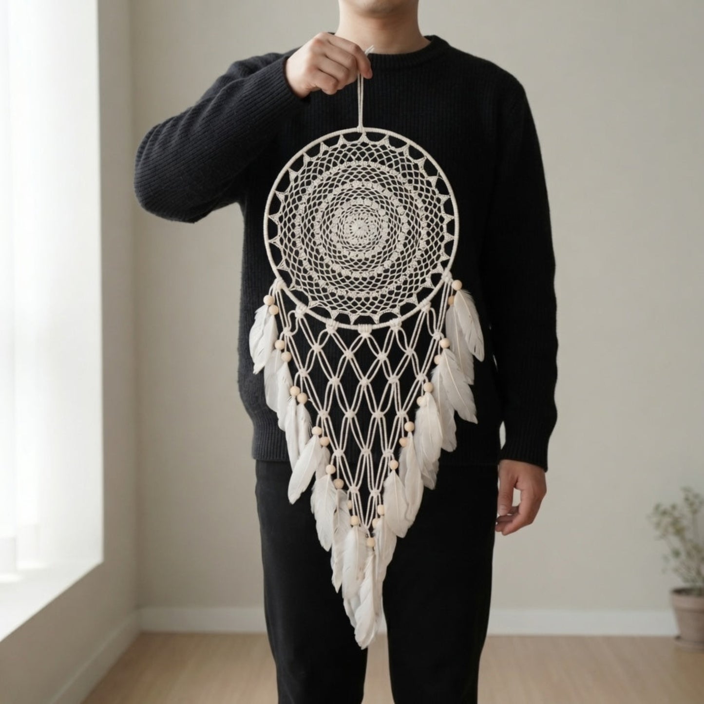 Person holding a large boho dreamcatcher wall hanging with crochet mandala and faux feather tail