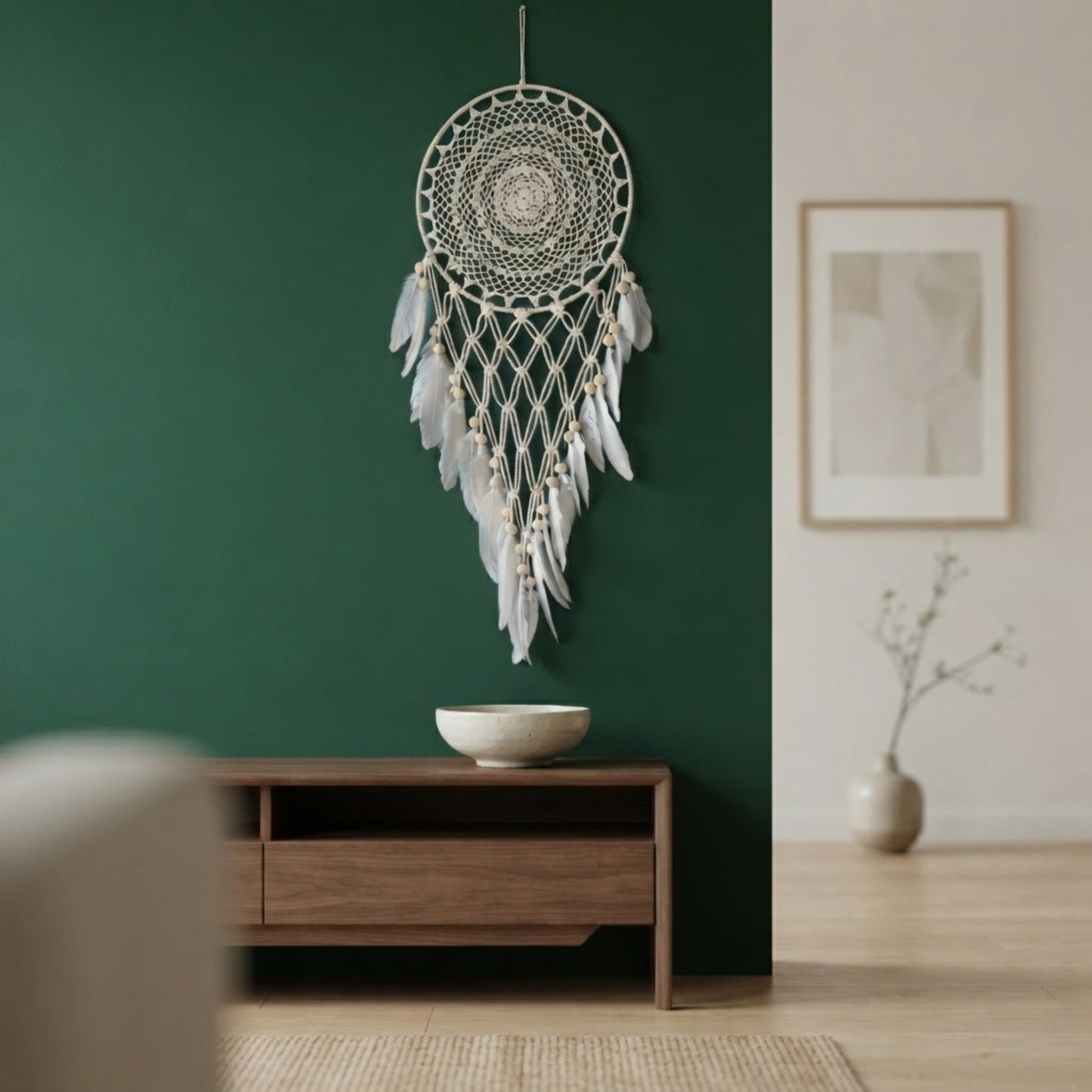 Boho macrame dreamcatcher with faux feather decor mounted on a deep green living room wall