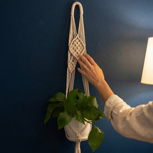 Hand touching lace flower medallion weave on macrame plant hanger against dark navy blue wall