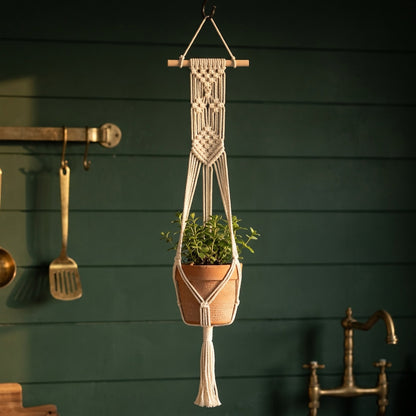 Macrame hanging planter with wooden stick and tassels on dark green wall farmhouse style indoor plant decor