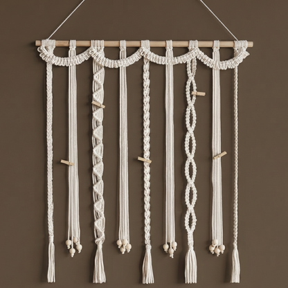 Suspension murale en macramé blanc crème avec tige en bois, perles en bois et pompons sur fond taupe